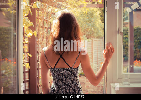 Una giovane donna è in piedi sulla porta della sua cucina e guardando il giardino di sunrise Foto Stock