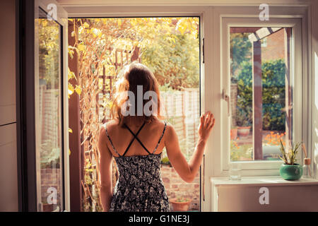 Una giovane donna è in piedi sulla porta della sua cucina e guardando il giardino di sunrise Foto Stock