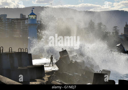 Silhouette di uomo e cane che vengono spruzzati da una grande onda su un molo vicino al faro in Wollongong, NSW, Australia Foto Stock