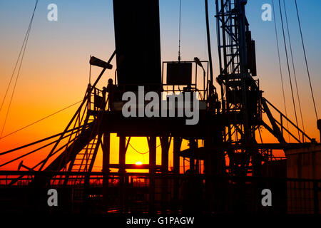 La sera del giacimento petrolifero, unità di pompaggio e la silhouette di oilfield derrick Foto Stock