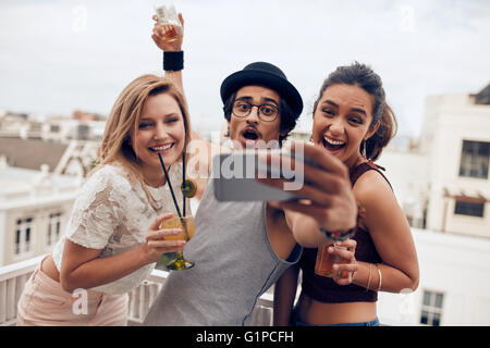 Emozionato i giovani prendendo autoritratto con telefono cellulare durante una festa. Felice giovane uomo e donna prendendo autoritratto a ro Foto Stock