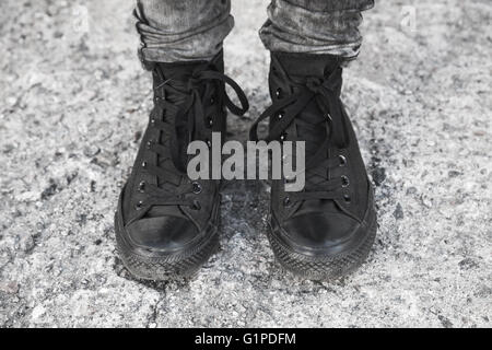 Adolescente piedi in nero gumshoes permanente sulla ruvida pavimento in calcestruzzo Foto Stock