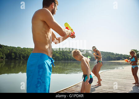 La famiglia felice con bambini la spruzzatura di acqua per ogni altro al lago Foto Stock