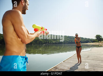 Coppia felice in un lago di spruzzatura di ogni altro con una pistola ad acqua in estate Foto Stock