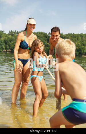 Famiglia avente il divertimento e la riproduzione di tiro della fune sul lago in estate Foto Stock