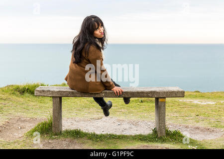 Giovane donna facendo quirky espressione mentre è seduto su una panchina. Le Bianche Scogliere di Dover, Dover, Kent, Regno Unito Foto Stock