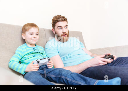 Stupito padre Felice i giochi per computer con suo figlio sul divano di casa Foto Stock