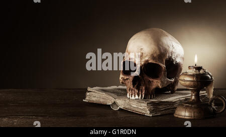 Cranio umano, candela accesa e aprire il libro antico su un vecchio tavolo di legno, la conoscenza e il concetto di alfabetizzazione Foto Stock