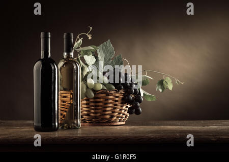 Le bottiglie di vino, uva e foglie di vite in un cesto su una tavola in legno rustico, still life Foto Stock