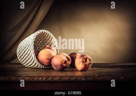 Mature le pesche in un cestello di bianco su una tavola in legno rustico e appoggiatelo sul background, frutto ancora vita Foto Stock