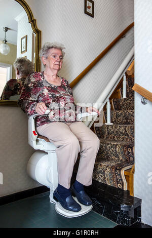 Donna anziana utilizzando montascale / stair glider, il dispositivo meccanico per il sollevamento di persone su e giù per le scale di casa Foto Stock