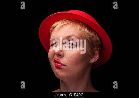 Orizzontale vista anteriore ritratto di una giovane donna bionda con Red Hat facendo una faccia su sfondo nero Foto Stock