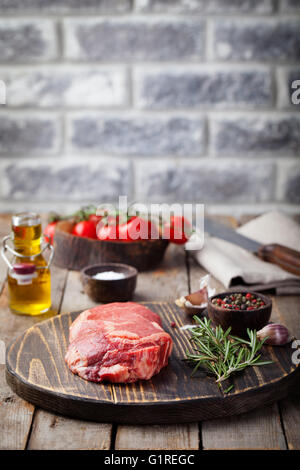 Crudo fresco di carne di manzo con sale e pepe, rosmarino e pomodori sul tagliere in legno scuro copia di sfondo spazio. Foto Stock