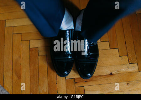 Bello fiducioso lo sposo in tuta blu mettendo sul nero scarpe, close-up Foto Stock