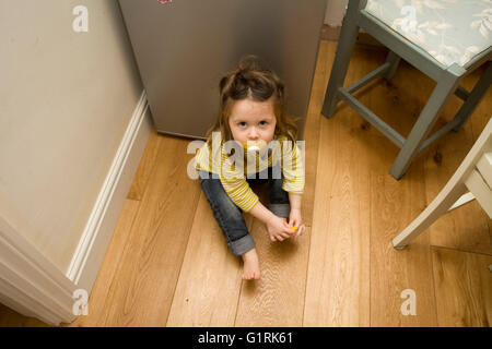 Femmina bambino seduto sul pavimento in cucina Foto Stock