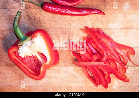 Peperone rosso, peperoncino e pepe fette, su di un tagliere di legno Foto Stock