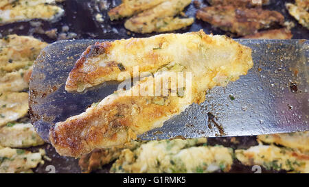 Bistrattato pesce persico, su una spatola di frittura, proprio di fronte a una pentola piena di erba pesce pastellati Foto Stock