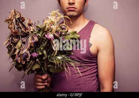 Un giovane triste è in possesso di un bouquet di morti e fiori appassiti Foto Stock