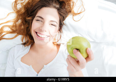 Donna sorridente azienda apple sul letto di casa Foto Stock