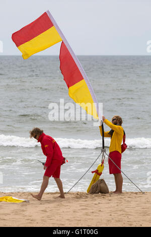 Bagnino di salvataggio che fissano il giallo e il rosso di flag che indicano una zona sicura di nuotare sulla spiaggia di Bournemouth nel Maggio Foto Stock