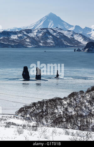 Bellissimo paesaggio della Kamchatka: vista su tre fratelli rocce nella baia Avacha e vulcano Vilyuchinsky in una giornata di sole Foto Stock