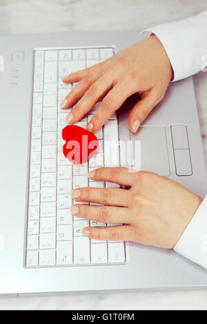 Una donna mano su di una tastiera di notebook con cuore rosso Foto Stock