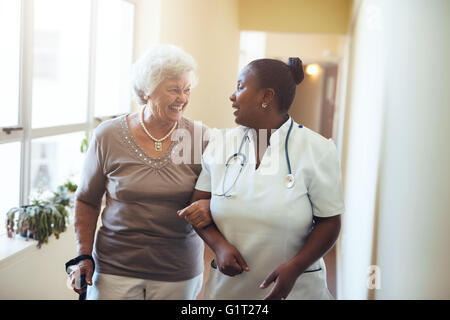 Senior Donna che cammina nella casa di cura supportato da un operatore sanitario. Un infermiere che assiste la donna senior. Foto Stock