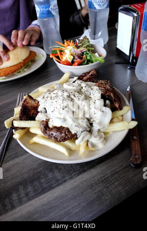 Una piastra di manzo con salsa di funghi e i chip con una ciotola di insalata greca e schnitzel di pollo Burger in background Foto Stock