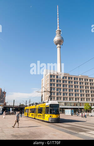 Berlino tram giallo viaggiando in Alexanderplatz Berlino Germania con la gente a piedi e la torre della TV Fernsehturm Foto Stock