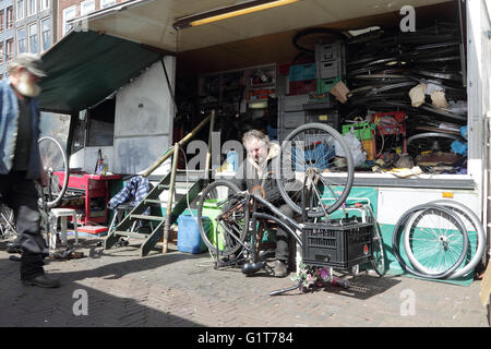 Uomo che ripara bicicletta nel suo negozio di riparazione sul mercato Waterlooplein ad Amsterdam, nei Paesi Bassi, l'Europa. Foto Stock