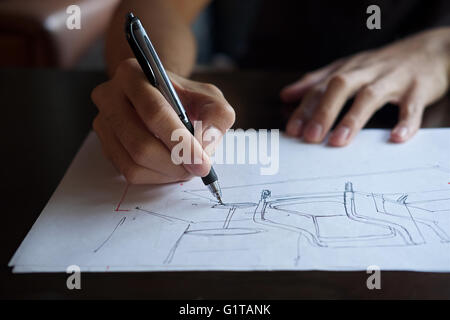 Mano di designer con la sua penna, progettando e delineando la sua idea su sketchbook Foto Stock