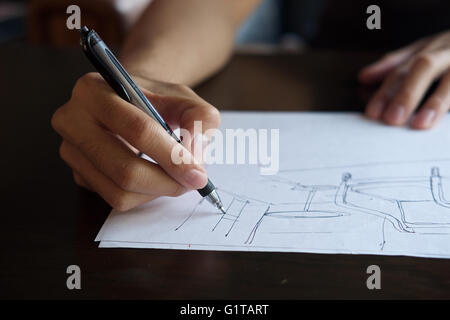 Mano di designer con la sua penna, progettando e delineando la sua idea su sketchbook Foto Stock