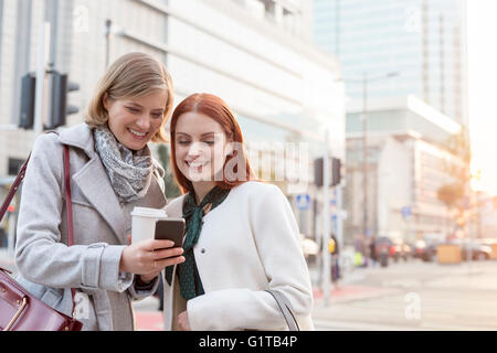 Sorridente imprenditrici sms e di bere il caffè sulla strada di città Foto Stock