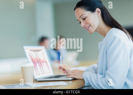 Sorridente imprenditrice lavora al computer portatile con caffè in sala conferenze Foto Stock