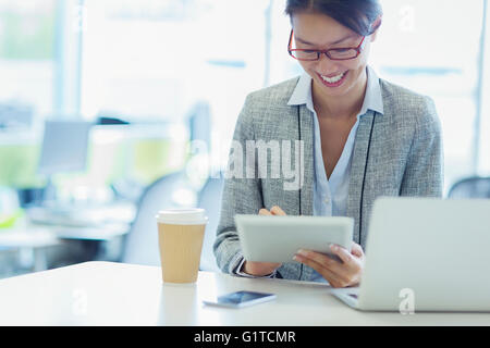 Imprenditrice sorridente con tavoletta digitale con caffè in ufficio Foto Stock