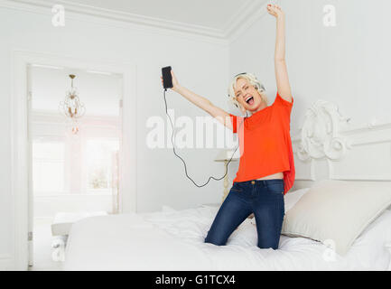 Giocoso donne inginocchiati sul letto ascoltando la musica con il lettore mp3 e cuffie Foto Stock