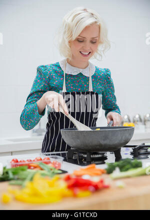 Donna sorridente nel grembiule cucina in cucina Foto Stock