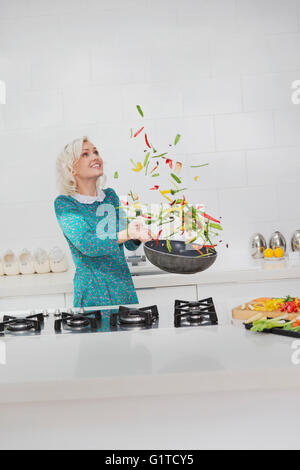 La donna la cottura di capovolgimento di verdure in padella in cucina Foto Stock