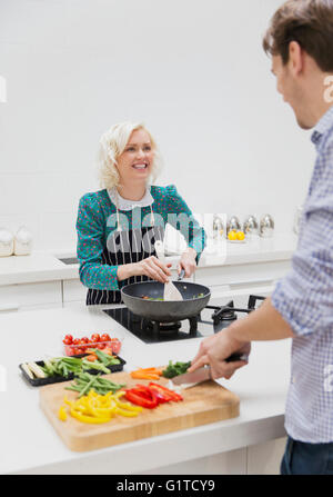 Coppia sorridente affettamento e cucina verdure in cucina Foto Stock