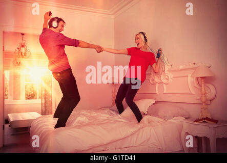 Giocoso coppia danzante sul letto ascoltando la musica con i lettori mp3 e cuffie Foto Stock