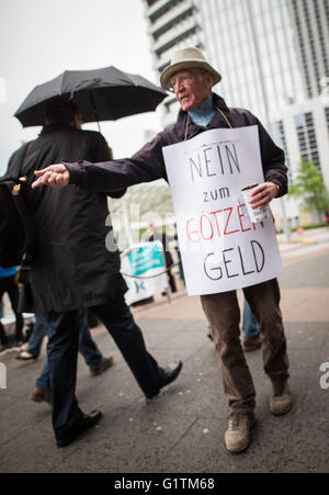 Un dimostrante porta un cartello che recita "No al falso dio denaro" mentre gettando delle monete ai piedi di Deutsche Bank azionisti all'entrata dell'assemblea degli azionisti del tedesco della società di servizi finanziari in Frankfurt am Main, Germania, 19 maggio 2016. Foto: FRANK RUMPENHORST/dpa Foto Stock