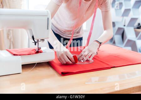 Primo piano della giovane donna sarta lavorando facendo pattern sul tessuto rosso Foto Stock
