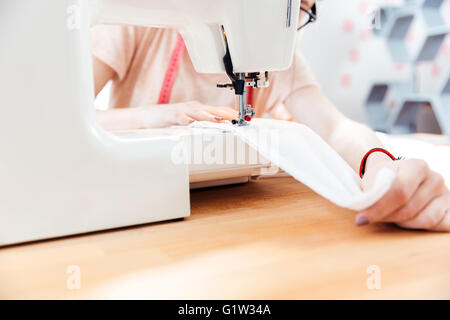 Primo piano della giovane sarta cuce vestiti con tessuto bianco Foto Stock