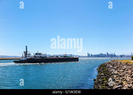 Un rimorchiatore a traino scortando una piccola nave cisterna Nave fuori del porto di Oakland il canale principale con lo skyline di San Francisco come sfondo Foto Stock