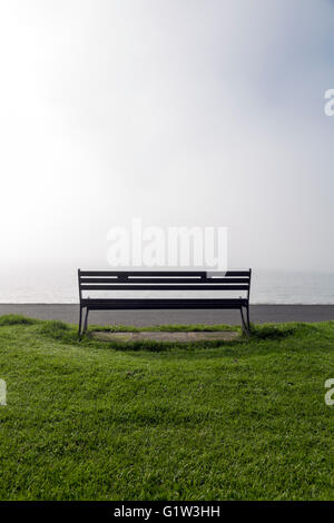 Una panca vuota che si affaccia su un mare nebbioso Foto Stock