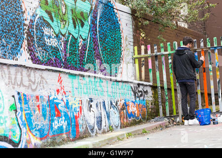 L'uomo dipinto graffiti sui pali da recinzione dal tunnel a Leake Street, Waterloo, Londra nel mese di aprile Foto Stock