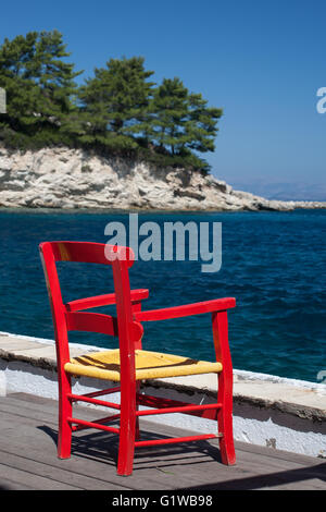 Rosso brillante sedia sul molo del grazioso e piccolo villaggio Harbourside di Loggos, Paxos, Grecia Foto Stock