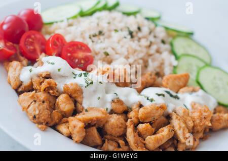 Gyros Il pollo su un piatto con riso, tzatziki medicazione e verdure - pomodoro, cetriolo Foto Stock