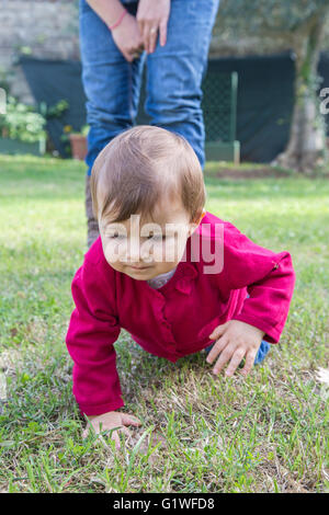 Un anno di età bambina guardando l'erba mentre strisciando nel giardino Foto Stock