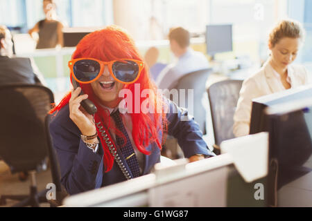 Ritratto di imprenditore giocoso indossando parrucca rosso ed enormi occhiali da sole in ufficio Foto Stock